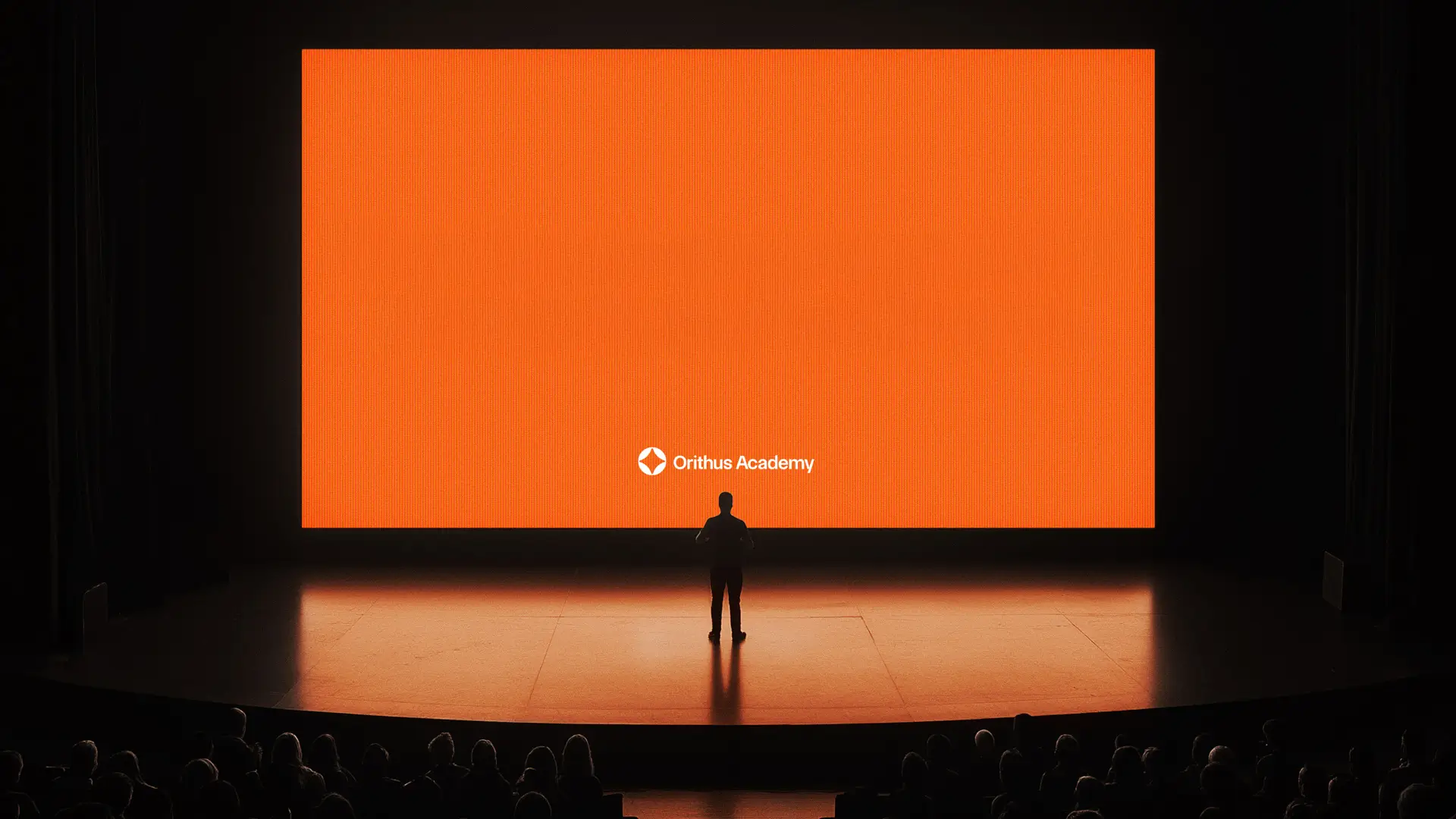 Homem em frente à tela laranja com o logo da Orithus Academy